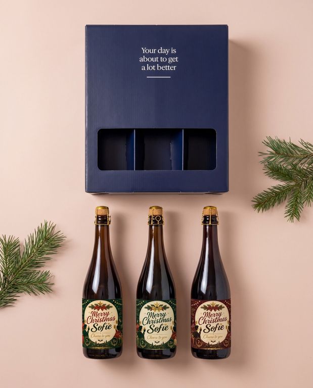 Bierpakket als kerstcadeau, drie flessen met een gepersonaliseerd kerstetiket naast de geschenkdoos